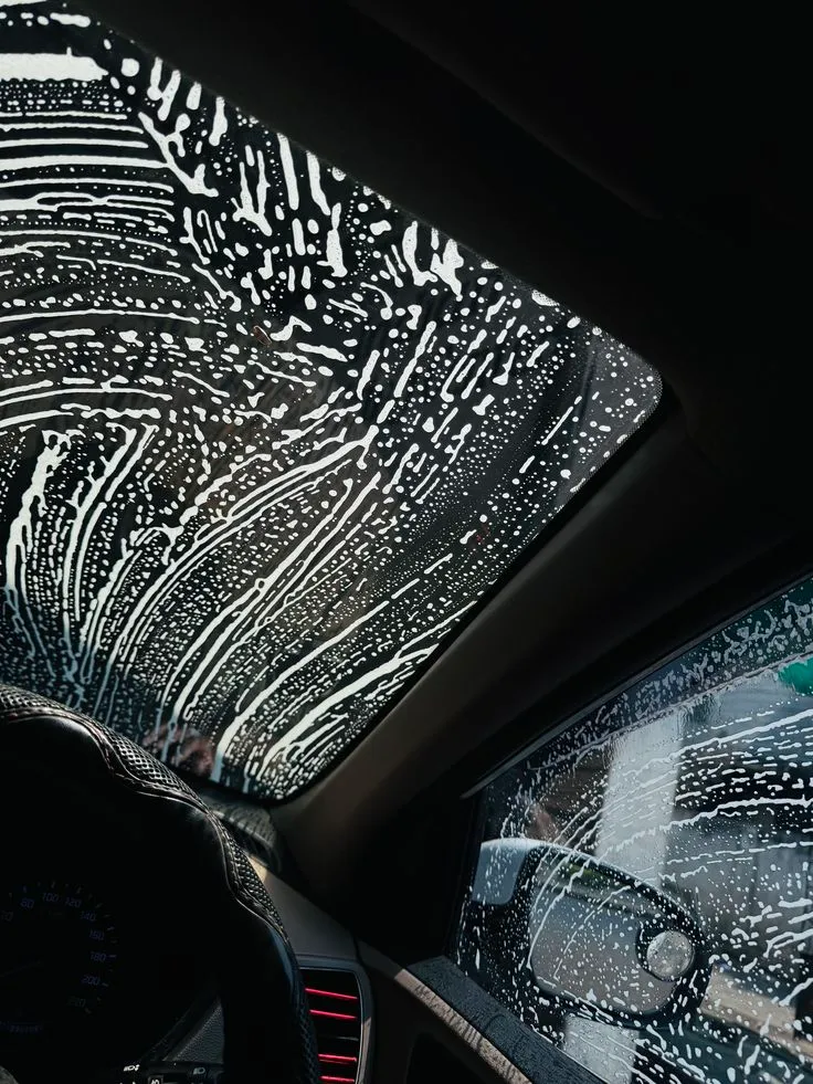 Windshield covered in wash suds, shot from inside the cabin mid-detail